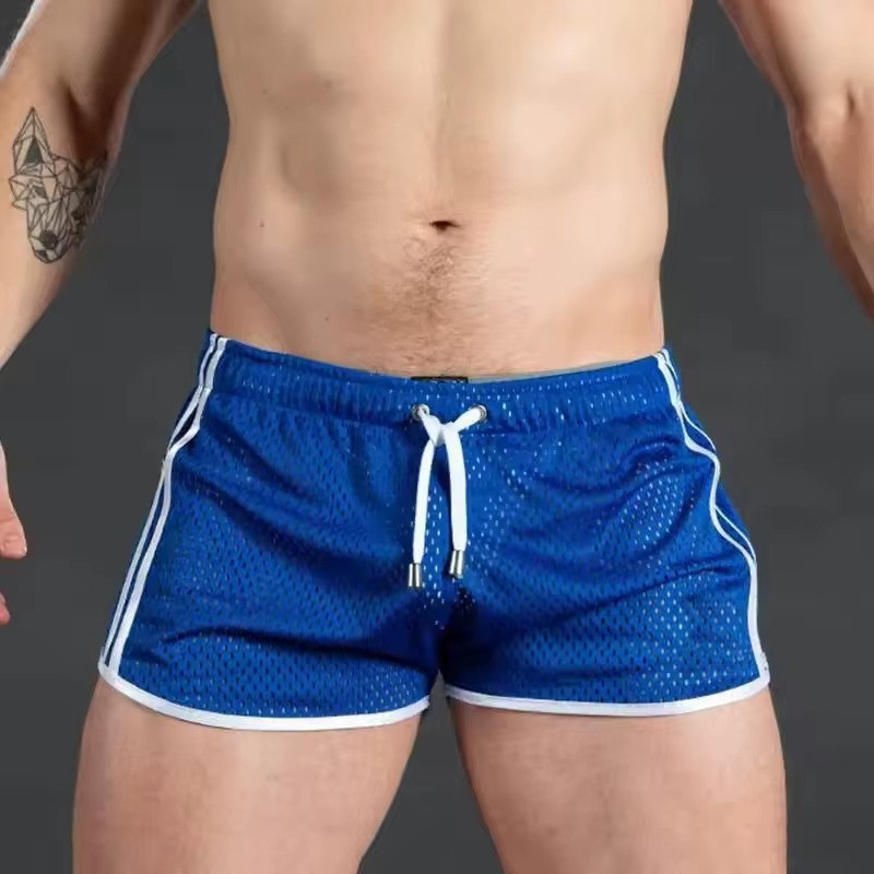 A close-up of a man's torso wearing blue athletic mesh shorts with white side stripes and a white drawstring, against a dark gray studio background.