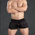 A muscular man wearing black mesh athletic shorts with a drawstring waist, standing with his arms crossed against a dark gray studio background.