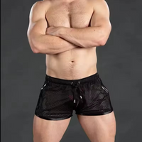 A muscular man wearing black mesh athletic shorts with a drawstring waist, standing with his arms crossed against a dark gray studio background.
