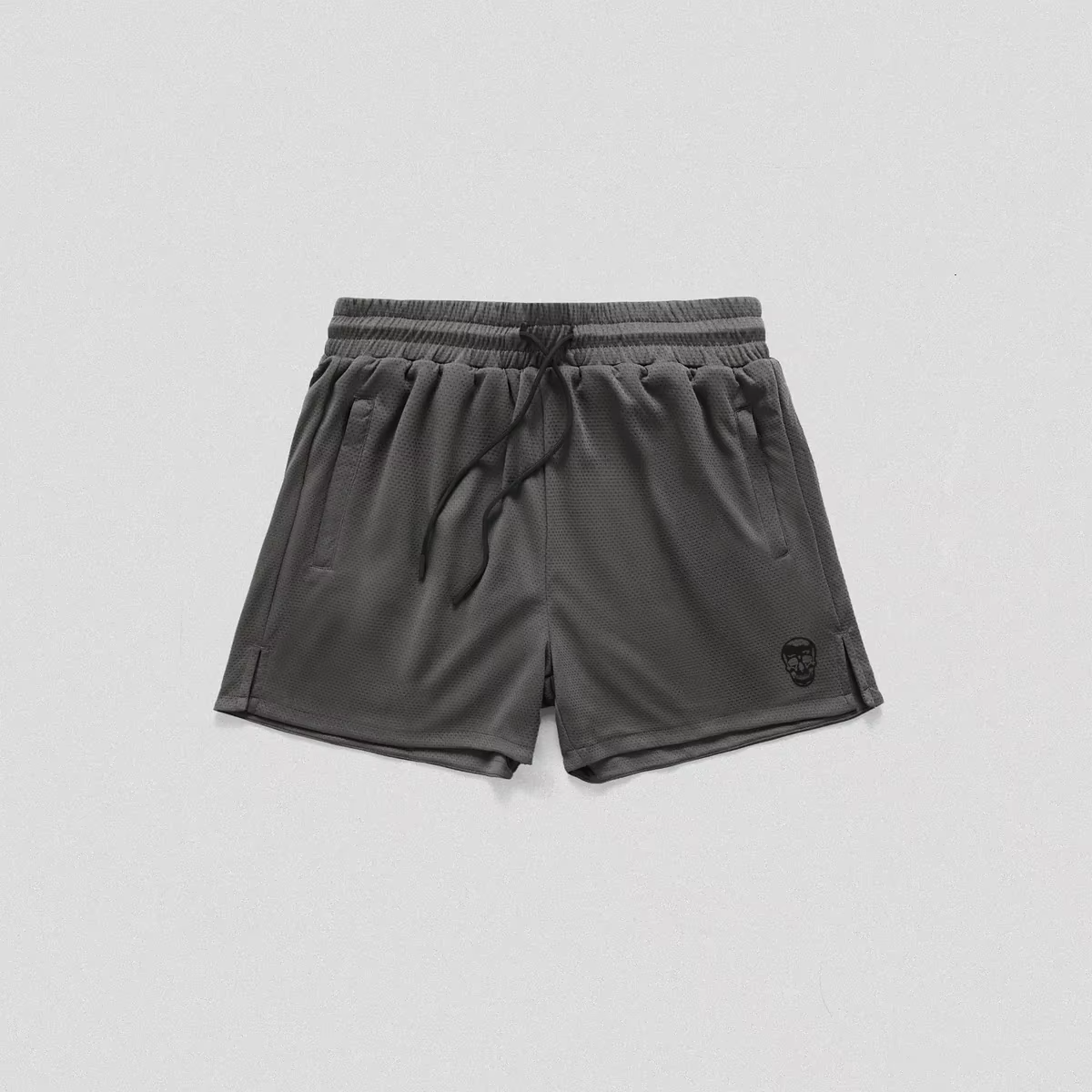 Dark gray athletic shorts with an elastic drawstring waist and a small black skull logo on the lower left leg, shown flat on a light gray background.