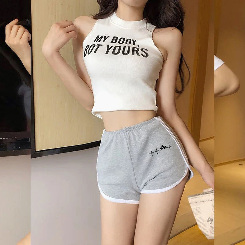 Person wearing a white tank top with text and gray shorts with a design, standing indoors.